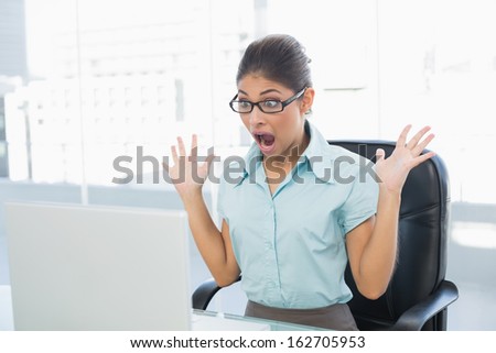 Shocked elegant young businesswoman looking at laptop in a bright office