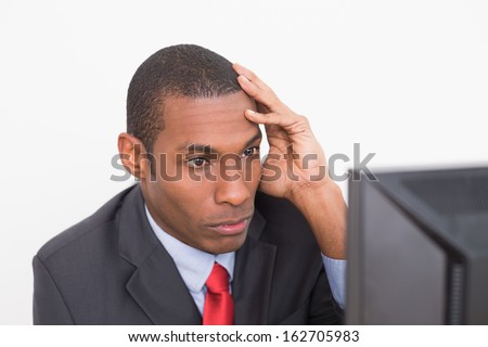 Close up of a serious young Afro businessman looking at computer against white background