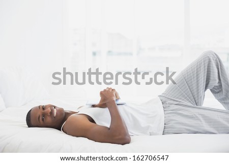 Portrait of a smiling young Afro man resting with digital tablet in bed at home