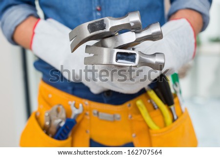 Close up mid section of a handyman holding hammers with tool belt around waist