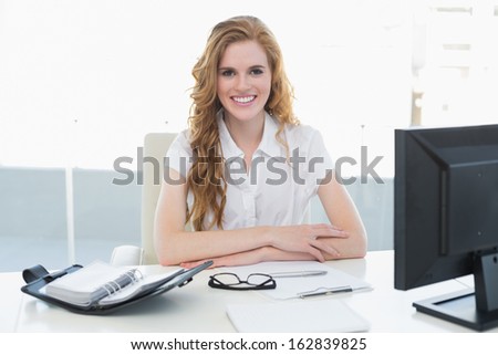 Portrait of a smiling businesswoman with computer sitting at desk in a bright office
