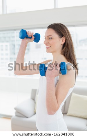 Side view of a fit young woman exercising with dumbbells in bright fitness studio