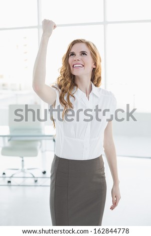 Cheerful elegant businesswoman cheering with hand raised in a bright office