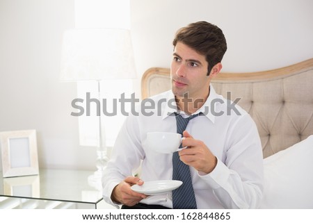 Serious well dressed man with a cup of tea in bed at home