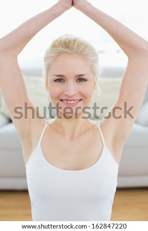 Toned young woman sitting with joined hands over head at fitness studio