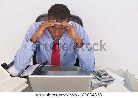 Frustrated young Afro businessman with head in hands at desk against white background