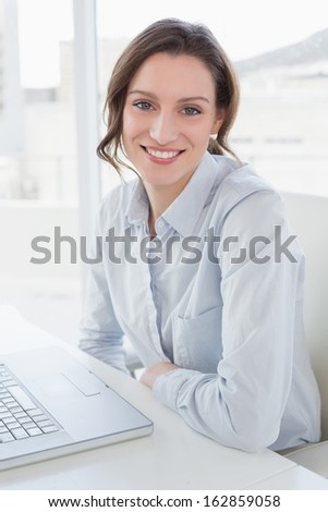 Portrait of a smiling young businesswoman with laptop in a bright office