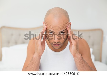 Close up of a young bald man suffering from headache in bed at home