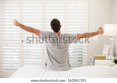 Rear View Of A Young Man Waking Up In Bed And Stretching His Arms