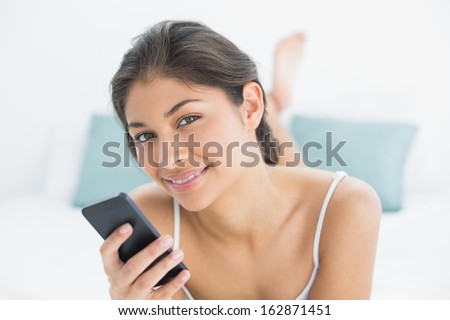 Portrait of a smiling young woman with mobile phone in bed at home