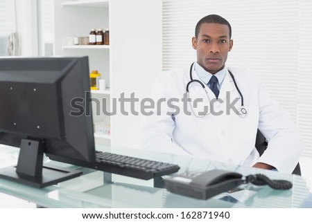 Portrait of a confident serious male doctor sitting with computer at medical office