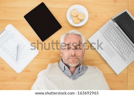 Overhead view of a mature man sleeping with electronics and biscuits on parquet floor at home