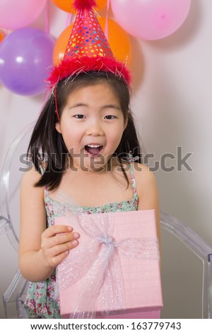 Close-up portrait of a shocked little girl opening gift box at her birthday party