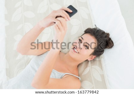 High angle view of a relaxed young woman looking at mobile phone in bed at home