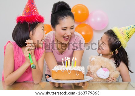 Close-up of cute little girls looking at mother with cake at a birthday party