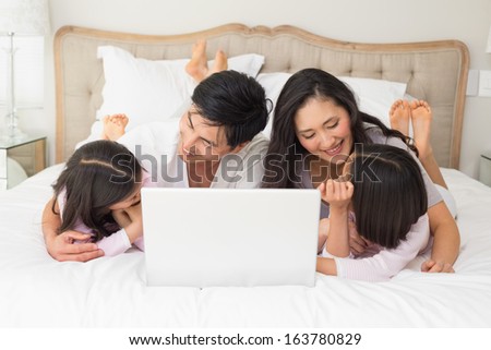 Happy relaxed family of four using laptop in bed at home
