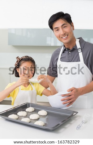 Portrait of a young man with his daughter preparing cookies in the kitchen at home
