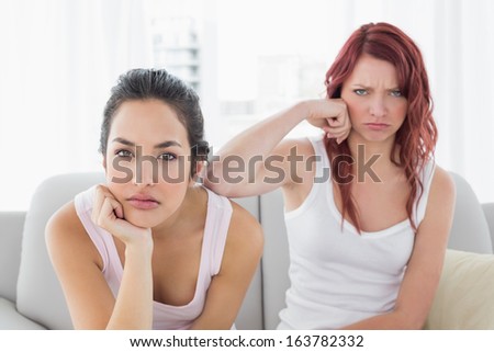 Portrait of unhappy young female friends not talking after argument at home on the couch