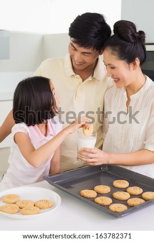 Young girl enjoying cookies and milk with parents in the kitchen