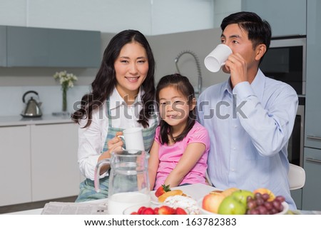 Portrait of a happy young girl enjoying breakfast with parents at table in the house