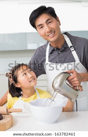 Portrait of a young man with his daughter using electric whisk into bowl in the kitchen at home