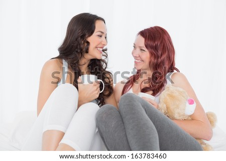 Cheerful relaxed female friends chatting over coffee in bed at home