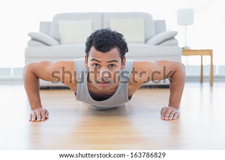 Portrait of a sporty young man doing push ups in the living room at house