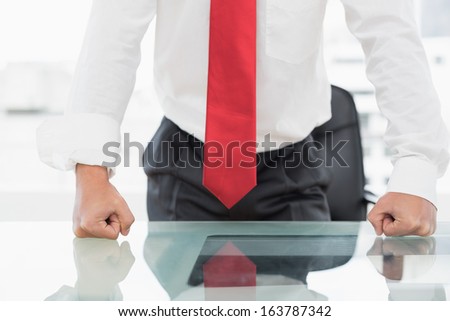 Close-up mid section of a well dressed businessman with clenched fists on the desk at office
