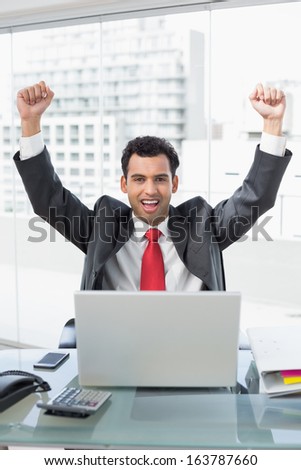Portrait of a businessman cheering with clenched fists in front of laptop at office desk