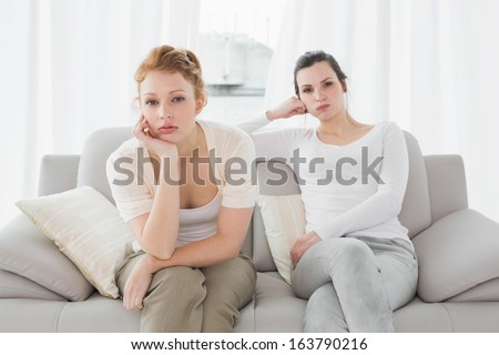 Unhappy young female friends not talking after argument at home on the couch