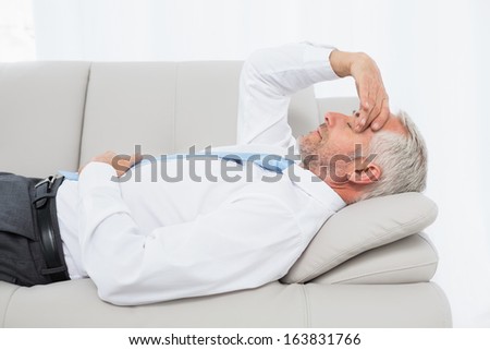 Side view of a tired mature businessman resting on sofa in the living room at home