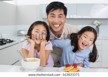 Portrait of a smiling man with happy two daughters having breakfast in the kitchen at home