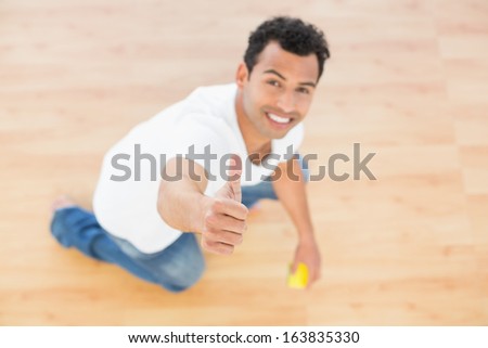 Portrait of a smiling young man cleaning the floor while gesturing thumbs up at house