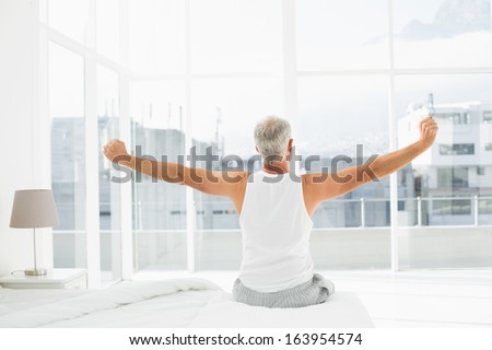 Rear view of a mature man waking up in bed and stretching his arms