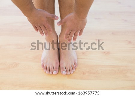 Close-up low section of a sporty young man stretching hands towards his feet on parquet floor