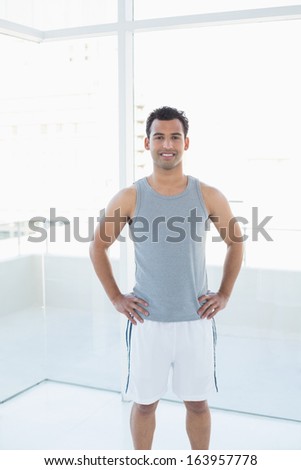 Portrait of a fit young man standing with hands on hips in a bright fitness studio