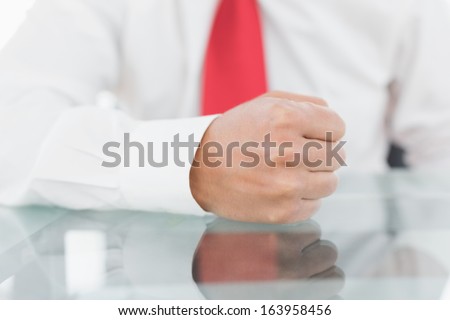 Close-up mid section of a well dressed businessman with clenched fist on the desk at office