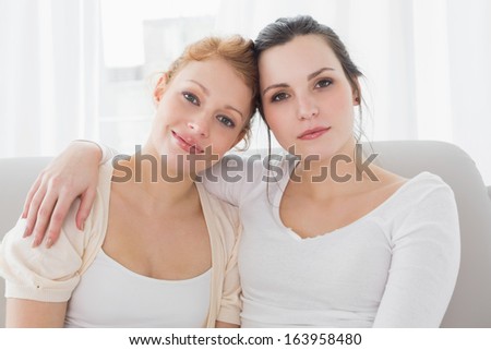 Portrait of smiling young female friends with arm around in the living room at home