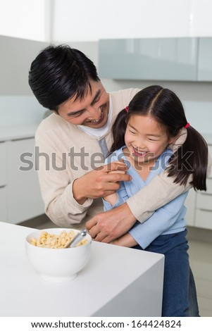 Cheerful father with young daughter having cereals in the kitchen at home