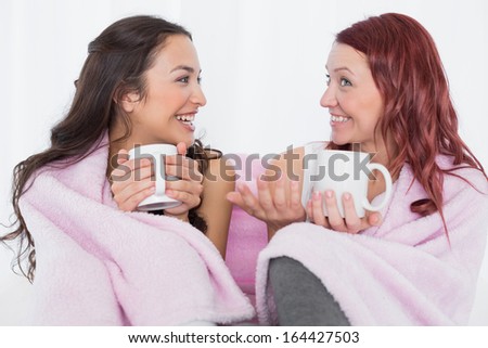 Happy young female friends with coffee cups in bed at home