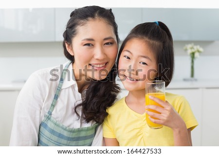 Portrait of a young girl holding orange juice with her mother in the kitchen at home