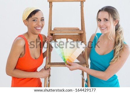 Portrait of two female friends with ladder choosing color for painting a room in new house
