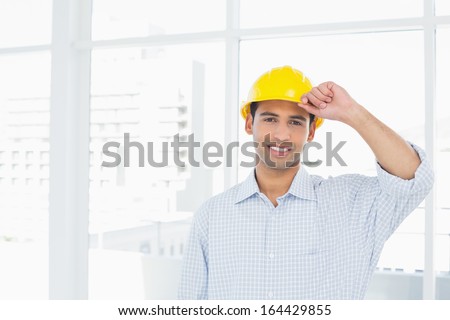 Portrait of a smiling handyman wearing a yellow hard hat against bright background