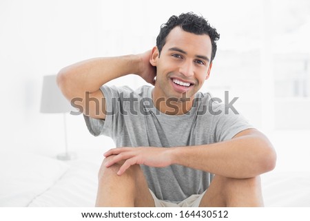 Portrait of a smiling young man sitting on bed at house