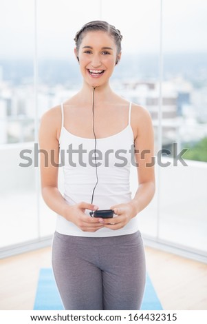Cheerful sporty model listening to music in bright fitness studio