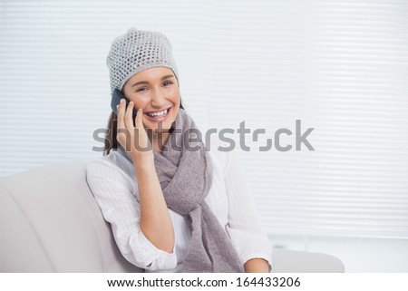 Pretty brunette with winter hat on having a phone call sitting on cosy sofa