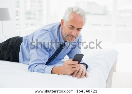 Smiling relaxed well dressed man text messaging in bed at home