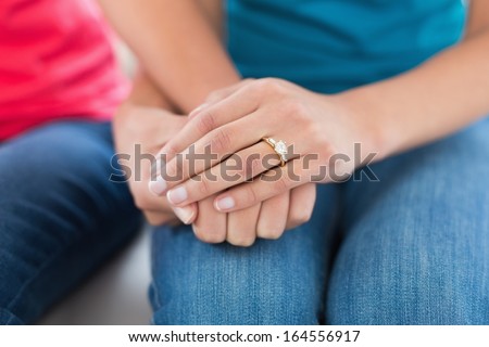 Close-up mid section of female friends holding hands at home on the couch