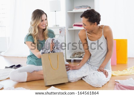 Two smiling young women sitting on the floor with shopping bag at home