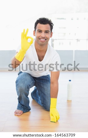 Portrait of a smiling young man cleaning the floor while gesturing okay sign at house